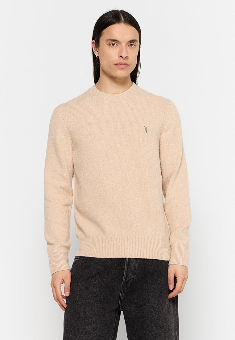 Beiger Strickpullover mit rundem Halsausschnitt sowie gerippten Bündchen und Saum. Verfügt über ein kleines Logo auf der Brust. Das Model trägt dunkle Jeans.