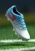 Blau-weißer Fußballschuh mit roten Akzenten, in der Luft über einem Rasenfeld mit weißer Linie und verstreuten Grasschnitt.