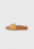 Braune und beige Slide-Sandale mit Wildleder-Oberriemen und flacher Gummisohle, fotografiert vor einem hellgrauen Hintergrund.