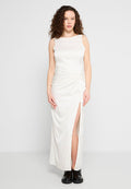Weißes Satin-Maxikleid mit ärmellosem Design, Knoten-Detail an der Taille und einem seitlichen Schlitz. Das Model trägt schwarze Schuhe.