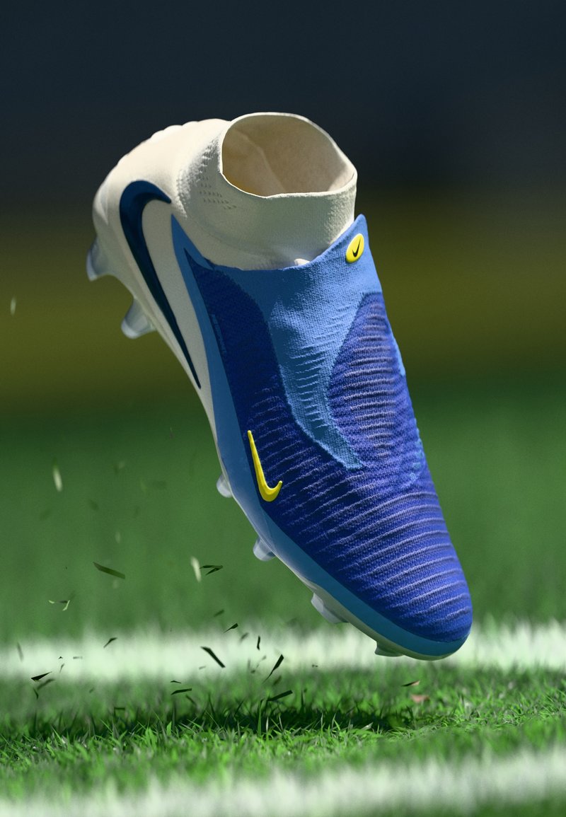 Blauer Fußballschuh mit strukturiertem Obermaterial, weißem Kragen, gelben Akzenten und einem stromlinienförmigen Design, schwebend über Gras mit Schutt.