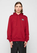 Roter Kapuzenpullover aus weichem Stoff, mit Kängurutasche, Kordelzügen, gerippten Bündchen und einem kleinen Markenpatch auf der Brust.