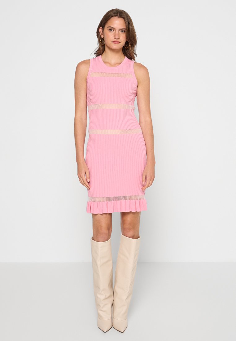 Rosa geripptes Kleid mit horizontalen transparenten Streifen, figurbetontem Schnitt und volantiertem Saum. Kombiniert mit beigen Stiefeln bis zum Knie.