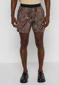 Braune Badehose mit einem Baumrindenmuster, elastischem Bund und glatter Textur. Getragen mit schwarzen Slippern.