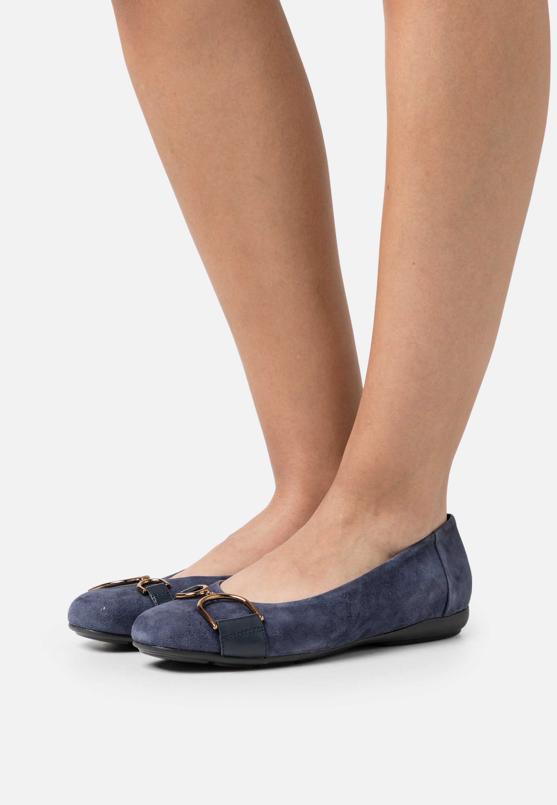 Navyblaue Wildleder-Ballerinas mit runder Zehenpartie, akzentuiert durch eine metallische Schnalle und eine flache Gummisohle. Glatte Textur überall.