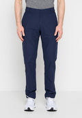 Mann trägt dunkelblaue, schmal geschnittene Hose und weiße Turnschuhe, steht vor einem schlichten hellen Hintergrund.
