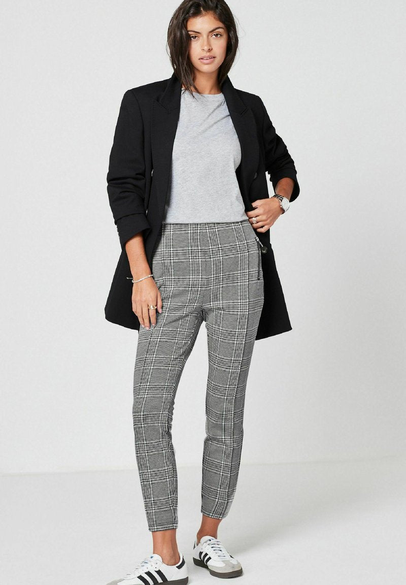Schwarze Blazer, graues T-Shirt und grau-weiße karierte, tapered Hose mit glatter Textur; kombiniert mit weißen Sneakern mit schwarzen Streifen.