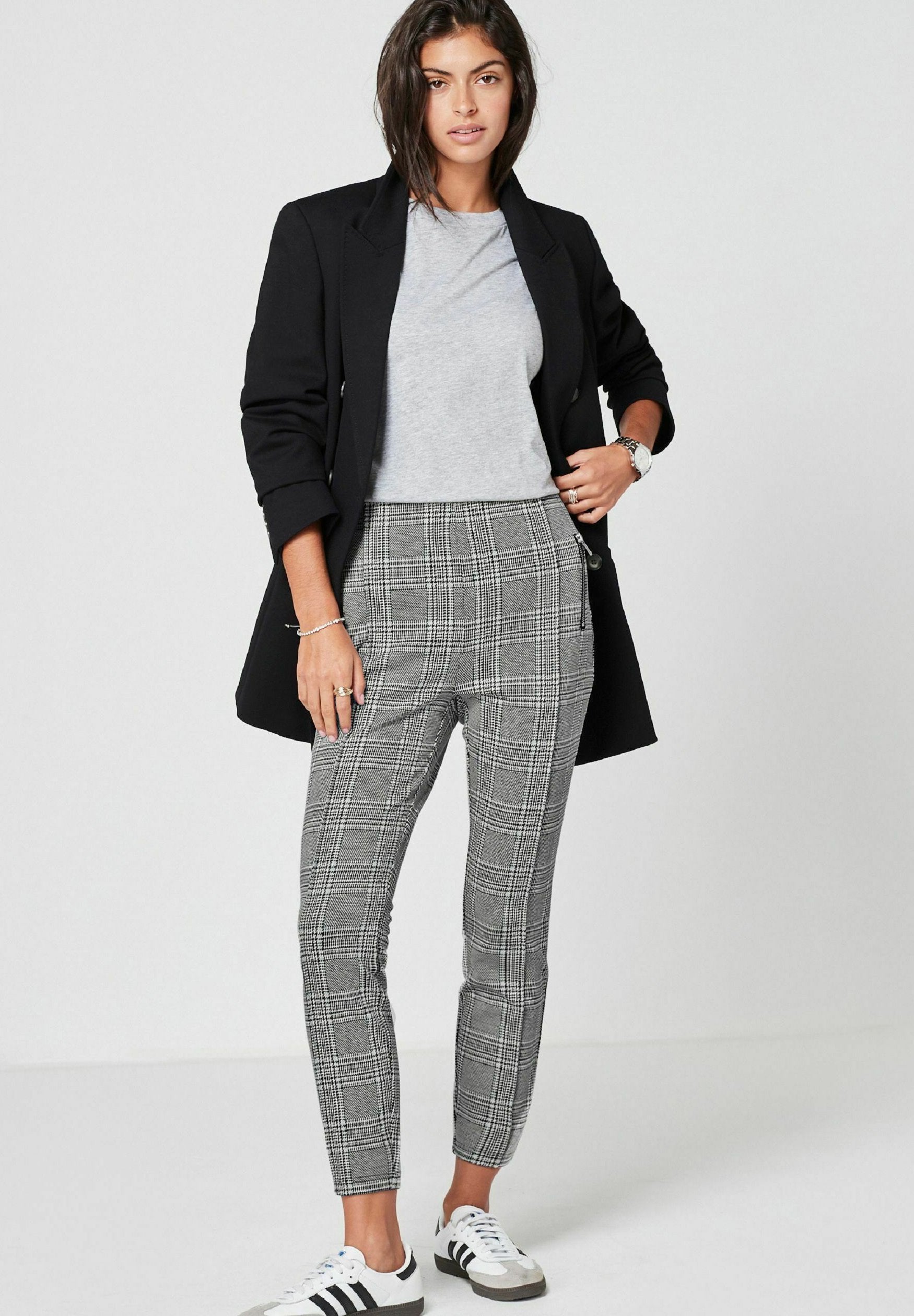 Schwarze Blazer, graues T-Shirt und grau-weiße karierte, tapered Hose mit glatter Textur; kombiniert mit weißen Sneakern mit schwarzen Streifen.