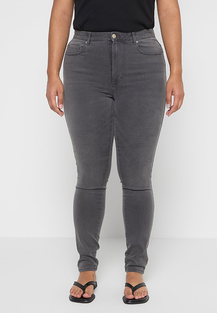 Graue Skinny-Jeans mit Fronttaschen, hoher Taille und glatter Textur, kombiniert mit schwarzen Sandalen.