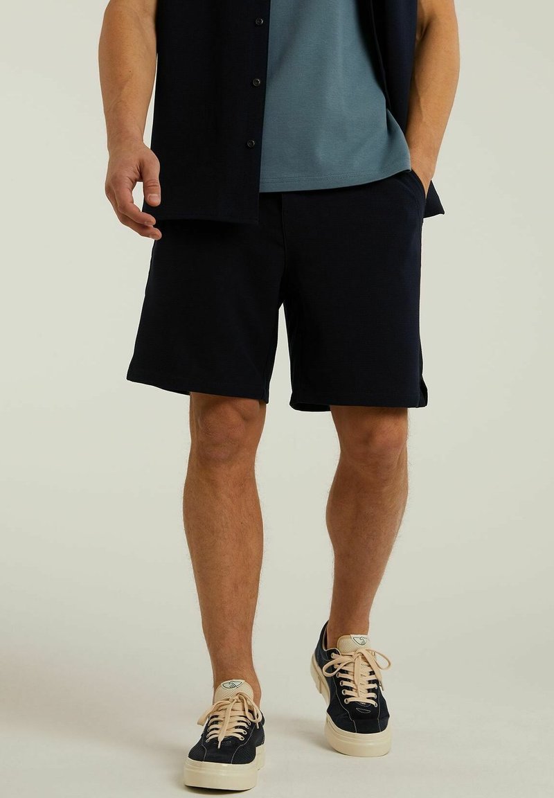 Marineblaue Shorts mit glatter Textur, Seitentaschen und einem elastischen Bund, kombiniert mit einem türkisfarbenen Rundhals-Shirt und marineblauen Sneakers.