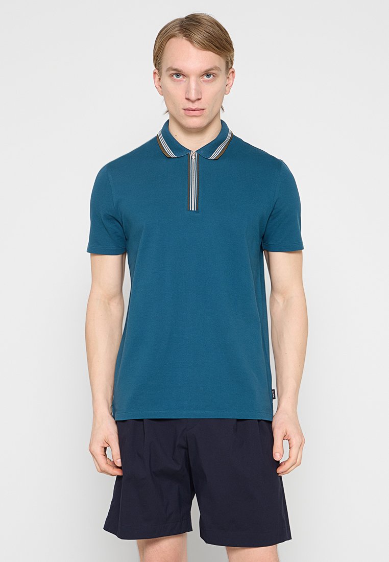 Türkisfarbenes Poloshirt mit gestreiftem Kragen, kurzen Ärmeln und geradem Schnitt. Wird mit dunklen Shorts getragen. Glatte Stoffstruktur, lässiges Design.