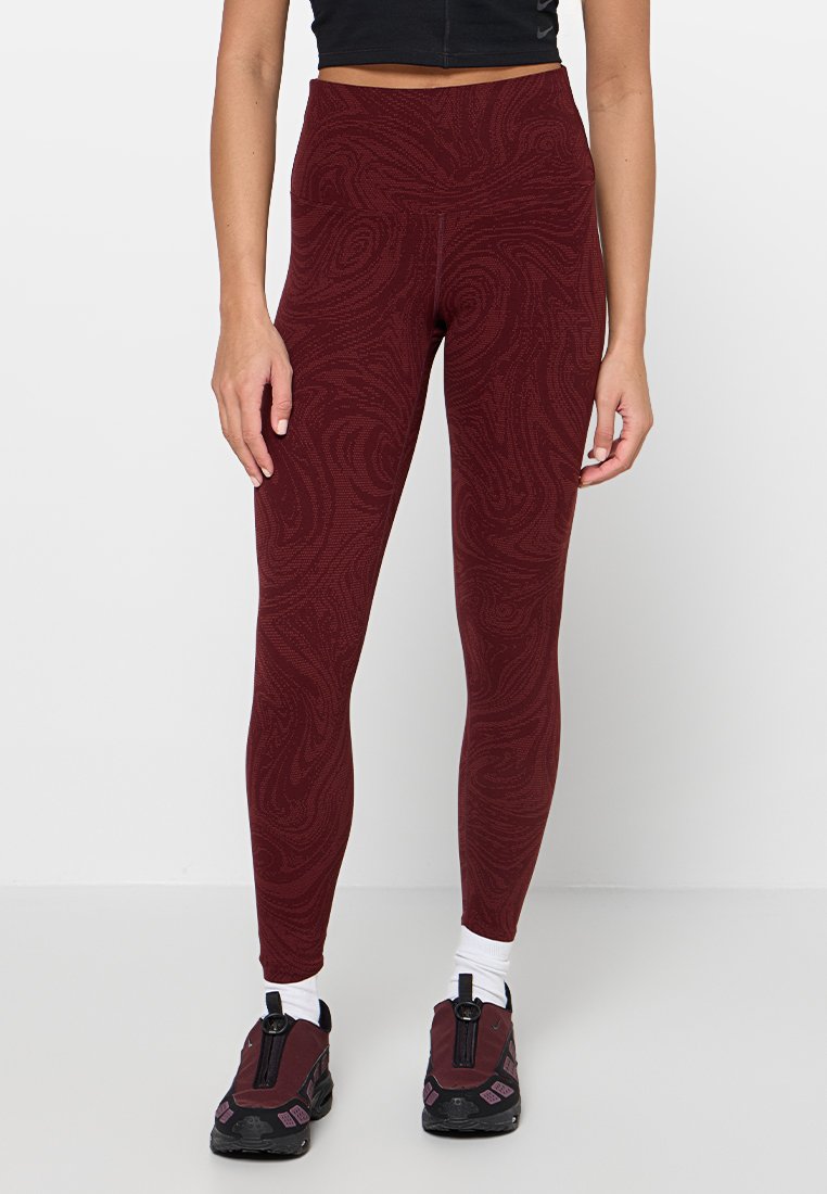 Burgunderfarbene gemusterte Leggings mit hohem Bund, aus strukturiertem Stoff, kombiniert mit schwarzen Sportschuhen und weißen Socken.