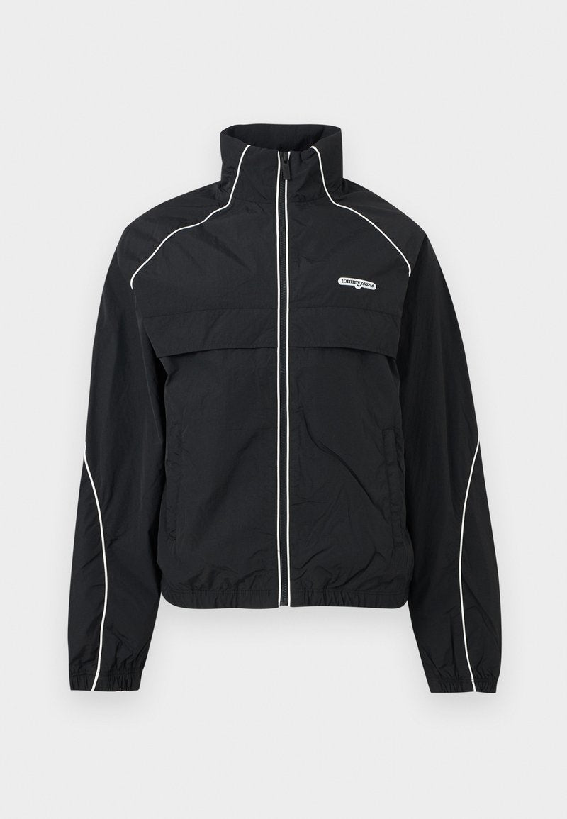 Schwarze Trainingsjacke mit Reißverschluss, weißen Kanten, hohem Kragen, elastischen Bündchen und "tommy jeans"-Logo auf der linken Brust.