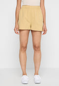 Beige Shorts mit elastischem Bund, aus leichtem Material gefertigt, mit lockerer Passform und bis zur Mitte des Oberschenkels reichend. Getragen mit weißen Sneakern.