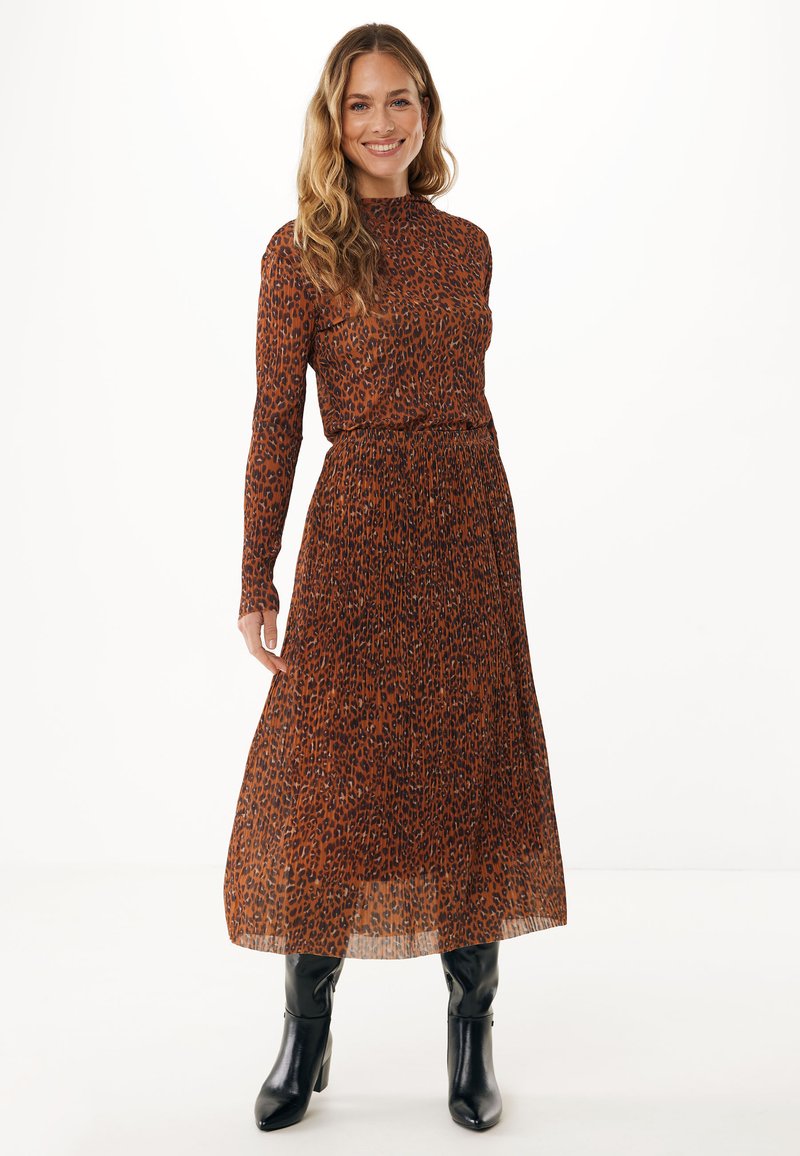 Langärmliges, hochgeschlossenes Kleid in orange-braun mit schwarzen Leopardenmustern; tailliert, mit fließendem Rock und kombiniert mit schwarzen knielangen Stiefeln.