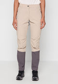 Person trägt beige und graue Outdoor-Hose und schwarze Wanderschuhe und steht vor einem schlichten weißen Hintergrund.