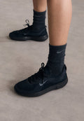 Schwarze Nike-Sneaker mit einem strukturierten Strickobermaterial, ausgestattet mit einem grauen Swoosh-Logo, kombiniert mit dunklen gerippten Socken. Flache Gummisohle.