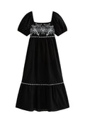 Schwarzes Kleid mit kurzen Puffärmeln, quadratischem Ausschnitt, weißer Blumenstickerei auf dem Oberteil und einem gestuften Rock mit welligem Saum.
