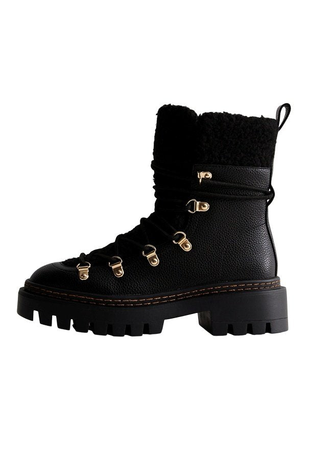 Schwarzer Lederstiefel mit strukturierter Oberfläche, plüschigem schwarzen Schaft, goldenen Elementen und einer kräftigen schwarzen Sohle mit Profilmuster.