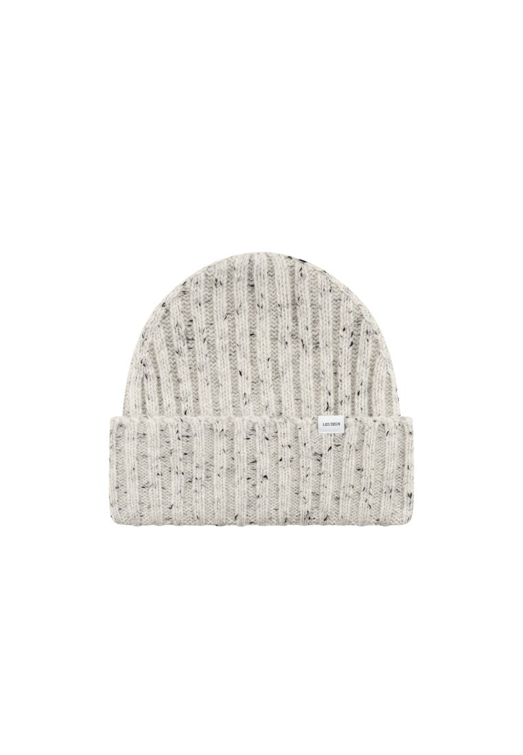 Gestrickte Mütze in Hellgrau mit schwarzen Punkten, mit umgeschlagenem Rand und einem kleinen weißen Etikett an der Seite. Weiches, strukturiertes Material.