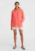 Korallefarbener Hoodie aus weichem Material mit einer Vorderasche, kombiniert mit hellen Batik-Shorts und Flip-Flops mit einem pinken Schleifendetail.