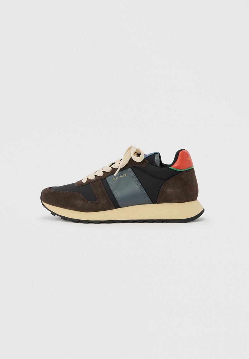 Niedriger Sneaker mit braunem Wildleder, marineblauen und türkisfarbenen Einsätzen, cremefarbenen Schnürsenkeln, beiger Sohle und rotem Fersenriemen vor weißem Hintergrund.