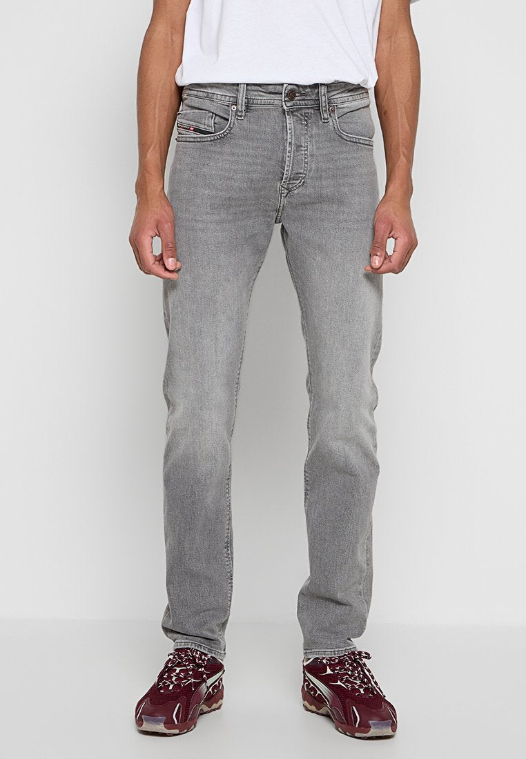 Graue Denim-Jeans mit geradem Schnitt, fünf Taschen und Metallknopfverschluss. Kombiniert mit einem weißen T-Shirt und weinroten Sneakers.