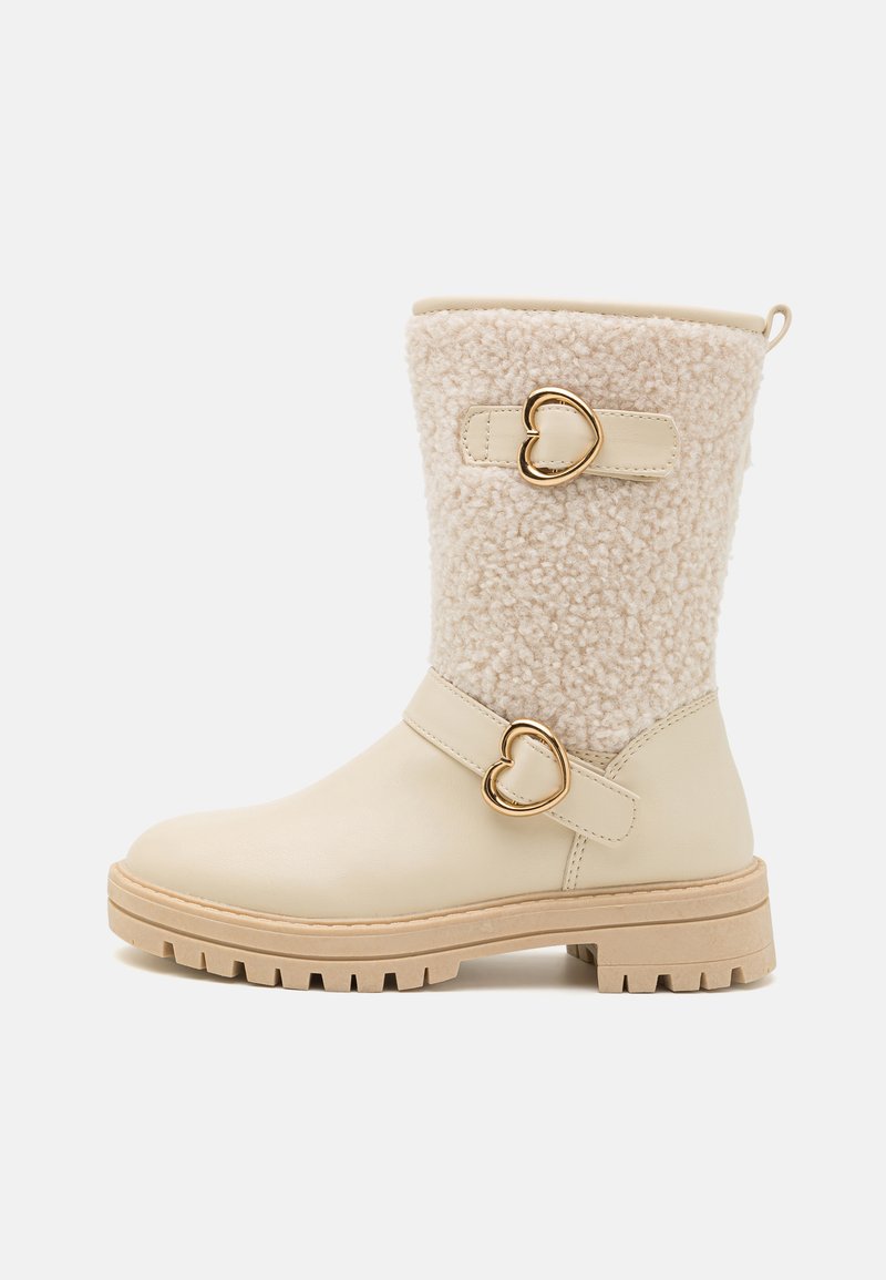 Beige Knöchelstiefel mit einem strukturierten cremefarbenen Fleece-Obermaterial, goldenen herzförmigen Akzenten und einer dicken beige Sohle. Seitliche Schnallendetails sind enthalten.