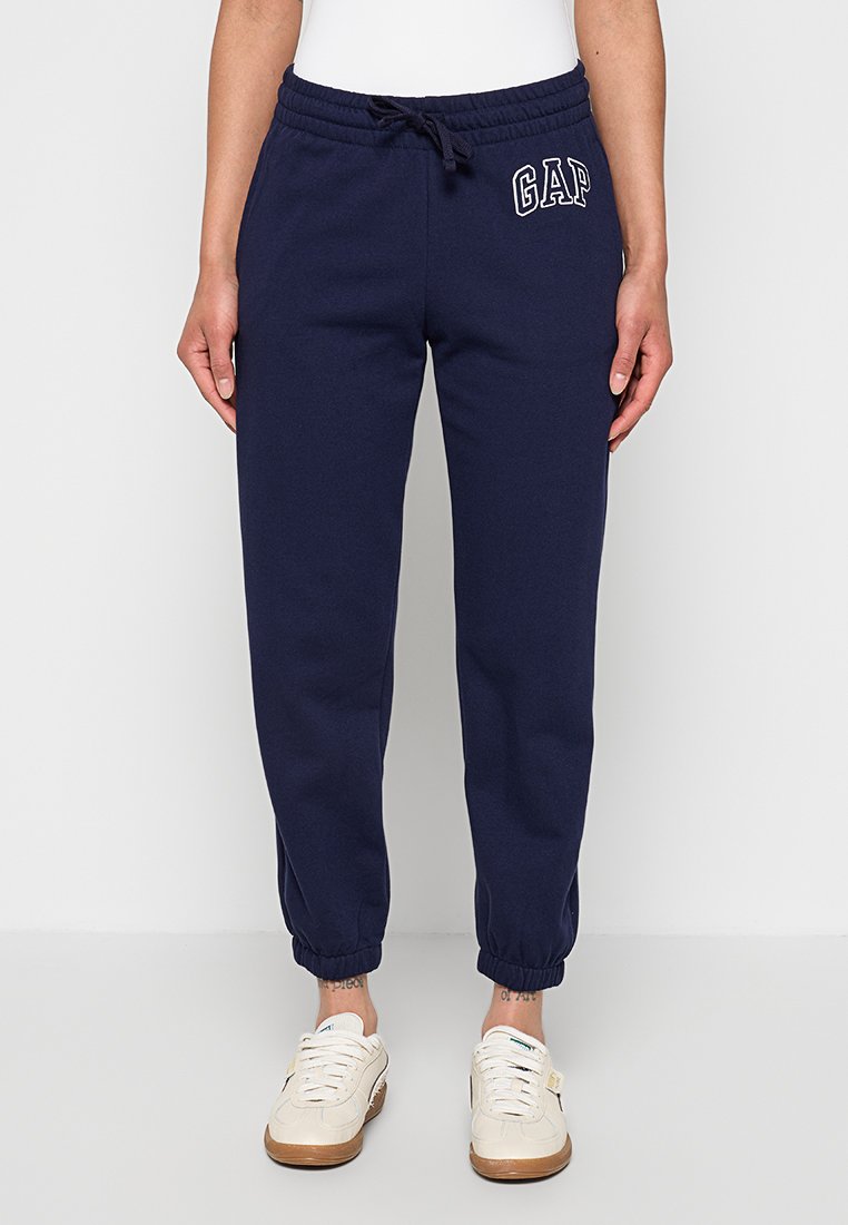 Marineblaue GAP-Sweatpants mit elastischem Bund und Bündchen, getragen mit weißen Sneakern und weißem Oberteil, Vorderansicht von der Taille bis zu den Füßen.