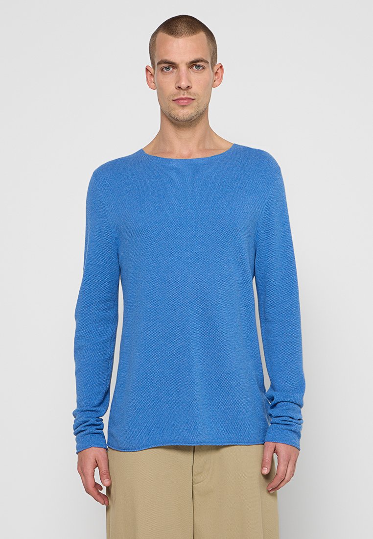 Blauer Langarmpullover mit strukturiertem Strick, weitem Rundhalsausschnitt und lockerer Passform. Mit schmalen Ärmeln und geradem Saum. Wird mit beigen Hosen getragen.