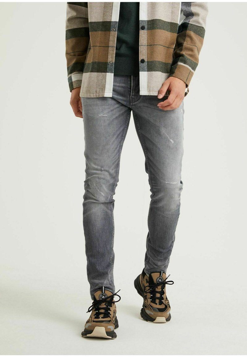 Graue Denim-Jeans im Slim-Fit, mit leichten Used-Effekten. Kombiniert mit einem karierten Hemd und gemusterten Sportschuhen.