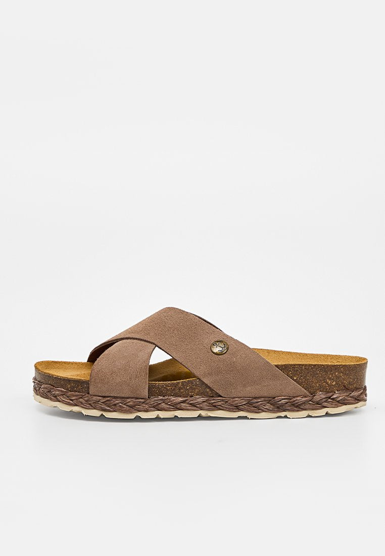 Brauner Veloursleder-Pantolette mit gekreuzten Riemen, gepolsterter Korksohle, geflochtenem Rand und kleinem rundem Metallemblem am Riemen.