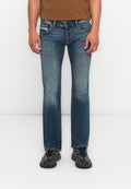 Mann in ausgebleichten blauen Straight-Leg-Jeans und schwarzen Sneakers, der vor einem schlichten weißen Hintergrund steht.