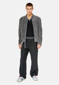 Grau gefütterte Kunstfelljacke, geripptes schwarzes Top, lockere schwarze Hose mit einem Stoffgürtel und sneakers mit metallischem Muster.