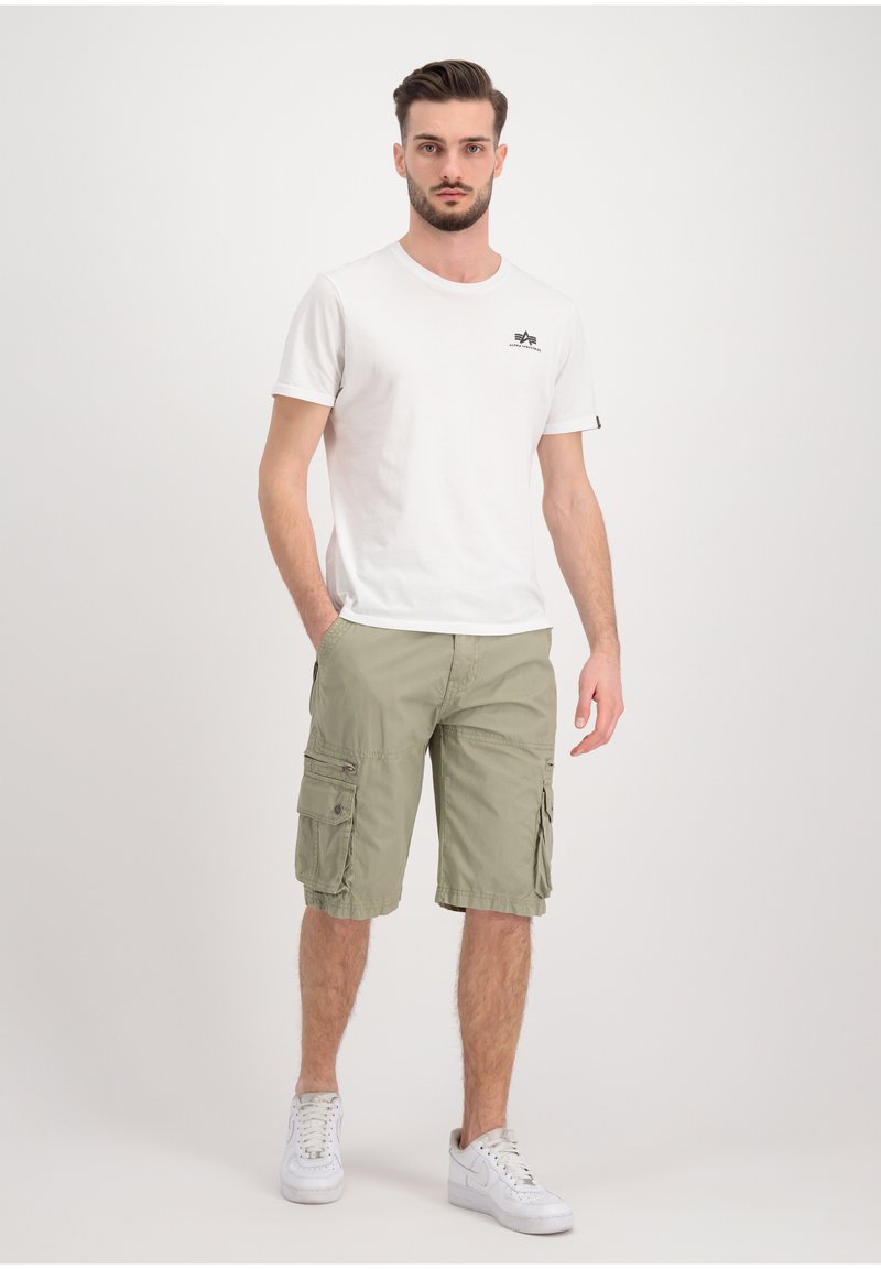 Weißes T-Shirt mit kurzen Ärmeln und kleinem schwarzem Logo, kombiniert mit hellolivgrünen Cargo-Shorts, die Seitentaschen und genähtes Detail aufweisen.
