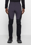 Mann trägt zweifarbige schwarze und dunkelgraue Outdoorhose mit Reißverschlusstaschen an den Seiten und schwarzen Sportschuhen, steht vor einem einfarbigen Hintergrund.