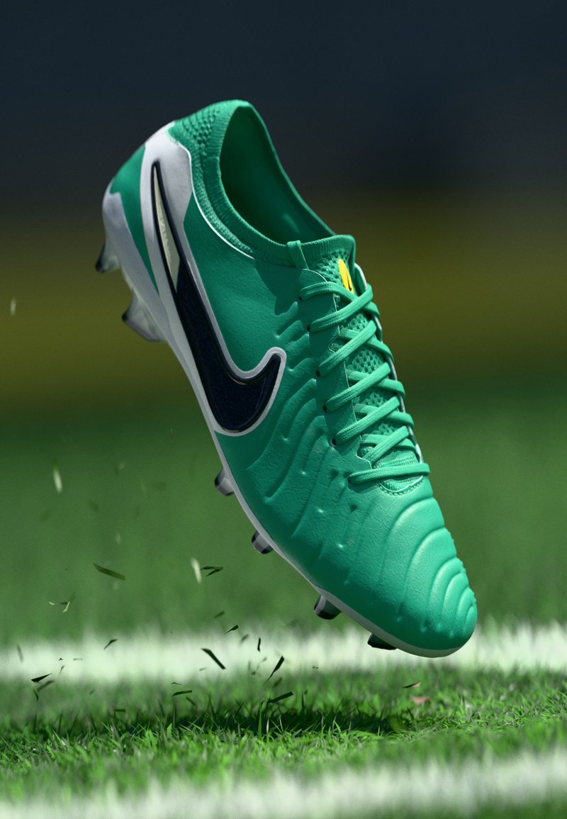 Grüner Fußballschuh mit strukturiertem Obermaterial, schwarzem Swoosh-Logo, gelben Akzenten und weißer Sohle. Über dem Gras erhoben mit herumfliegendem Schmutz.