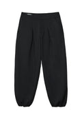 Schwarze Hose mit glatter Textur, die an der Vorderseite Falten, seitliche Taschen und ein tailliertes, elastisches Bein-Design aufweist.