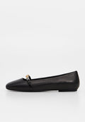 Schwarzer flacher Schuh mit spitzer Spitze und kleinem goldenen Ketten-Detail oben, fotografiert vor einfachem weißem Hintergrund.