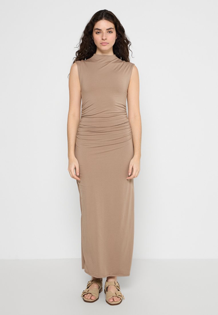 Beige ärmelloses Maxikleid mit tailliertem Oberteil und geraffter Taille. Weicher, glatter Stoff mit geradem Schnitt. Ein Paar braune Sandalen getragen.