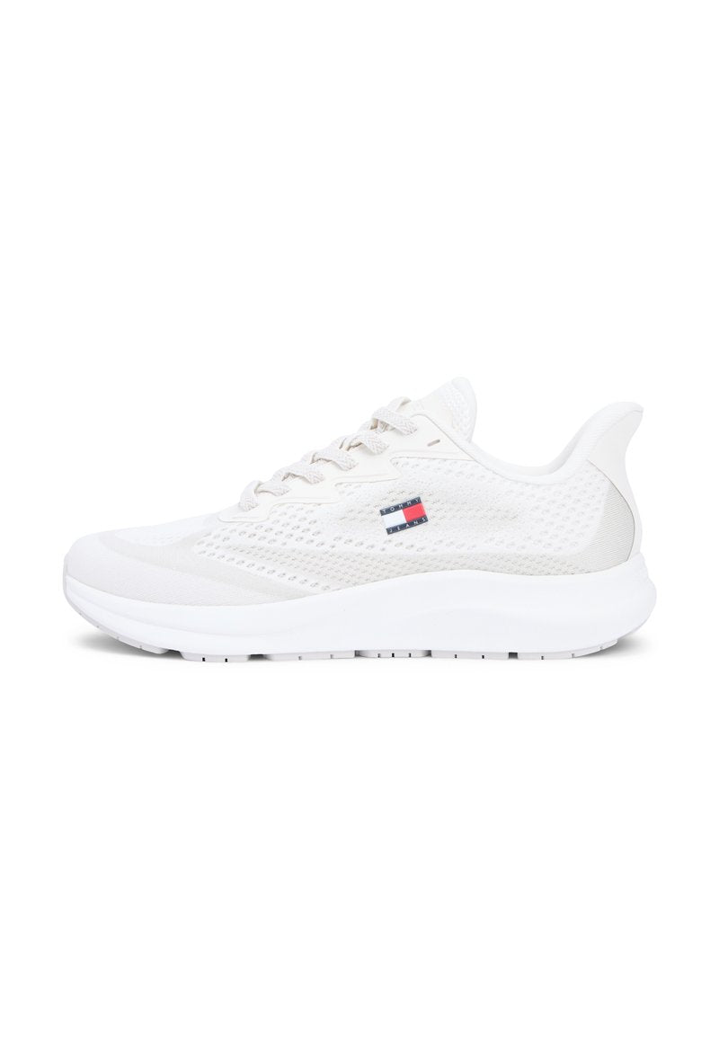 Weißer Sportschuh mit einem Mesh-Obermaterial, strukturierten Akzenten, rundem Zehenbereich, flachen Schnürsenkeln und einem Logoaufnäher in Rot, Weiß und Blau an der Seite.