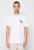Mann mit kurzen Haaren, der ein weißes T-Shirt mit den Buchstaben "LD" auf der Brust und beigefarbenen Hosen trägt, steht vor einem schlichten, hellen Hintergrund.