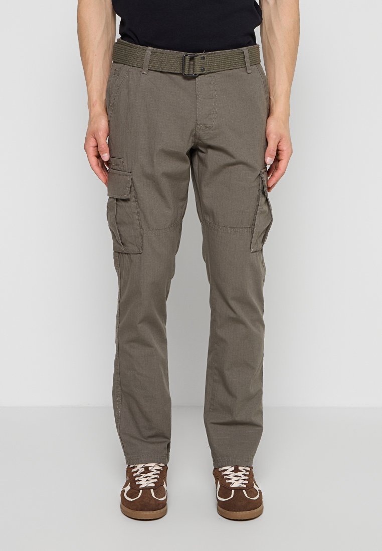 Mann trägt olivgrüne Cargohosen mit mehreren Taschen, passenden gewebten Gürtel, schwarzes Hemd und braune Schnürsneaker, steht aufrecht.