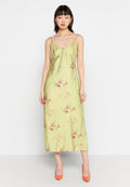 Hellgrünes Blumenkleid midi mit Spaghettiträgern, das eine geraffte Vorderseite und seitliche Schlitze aufweist. Getragen mit orangefarbenen Absätzen.