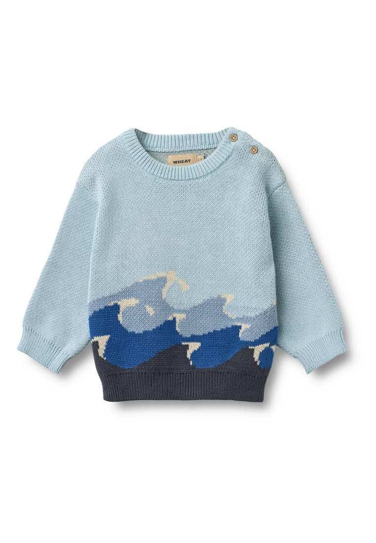 Hellblauer Strickpullover mit Wellenmuster in Blau- und Beigetönen, mit Rundhalsausschnitt und zwei Holzknöpfen an der Schulter.