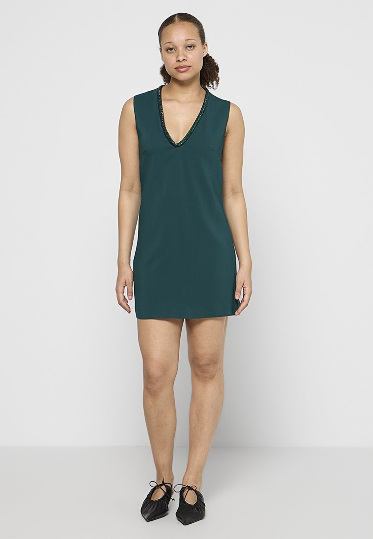 Türkises ärmelloses Kleid mit V-Ausschnitt und verzierten Halsabschluss; glatte Textur und gerade Passform, kombiniert mit schwarzen, weichen Ballettschuhen.