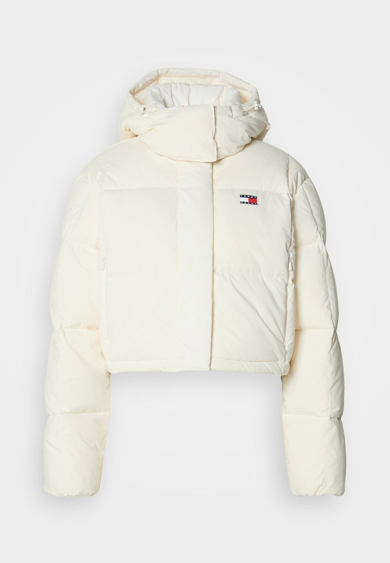 Kürzere, cremere Daunenjacke mit hohem Kragen und Kapuze mit Reißverschluss. Sie verfügt über ein rechteckiges Patch-Logo auf der Brust und gesteppte Abschnitte.