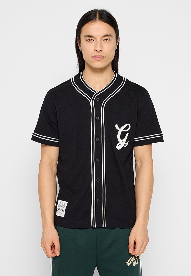 Schwarzes Kurzarmtrikot mit weißen Akzenten, Knopfverschluss vorne und einem "G"-Logo auf der linken Brust. Es hat einen runden Kragen und ein Seitenschild.