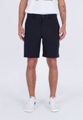 Mann in schwarzen knielangen Shorts, weißen Nike-Sneakern und einem weißen T-Shirt, der vor einem schlichten hellen Hintergrund steht.