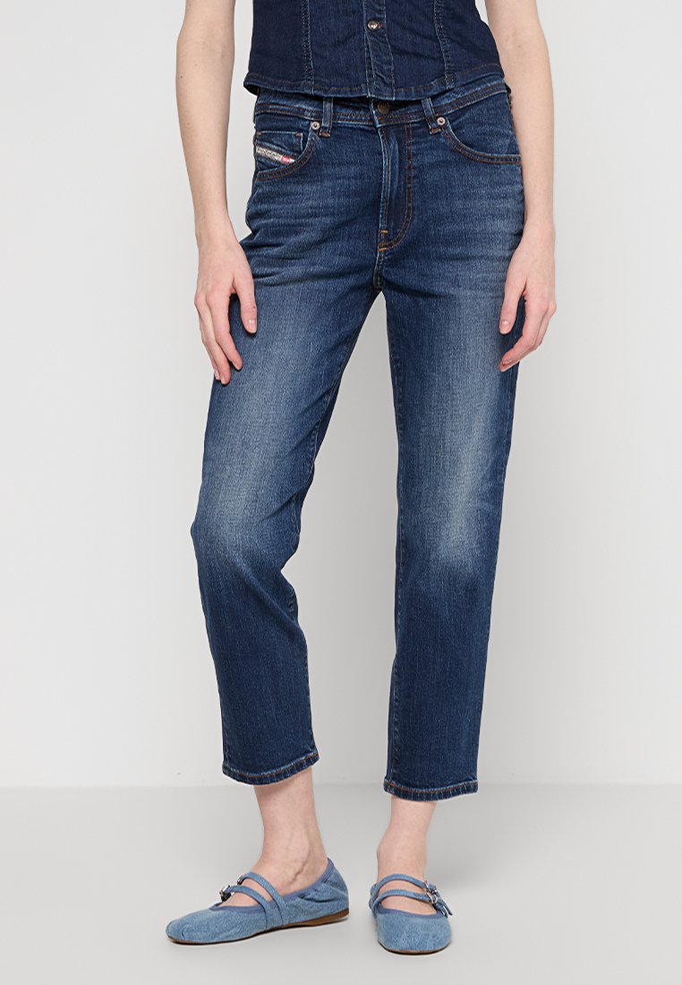Frau trägt dunkelblaue Denim-Jeans und ein passendes ärmelloses Denim-Top, kombiniert mit hellblauen Mary Jane Ballerinas.